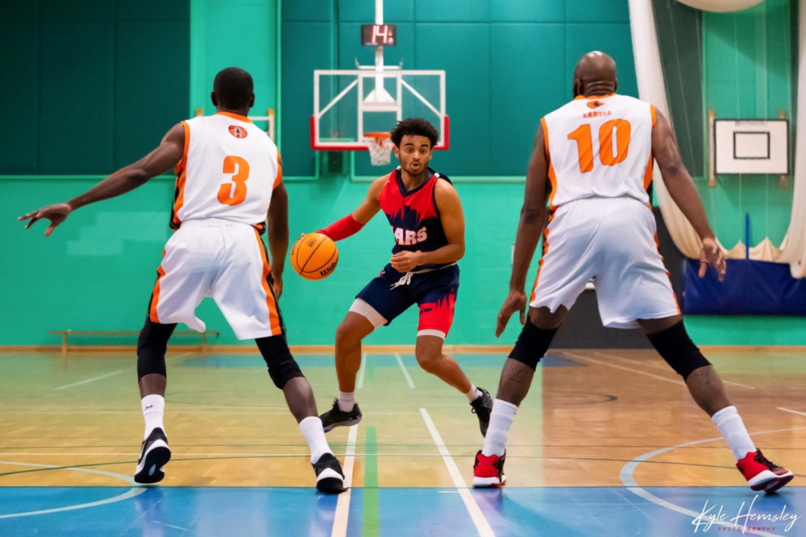 Photograph of a basketball player dribbling towards two defenders.