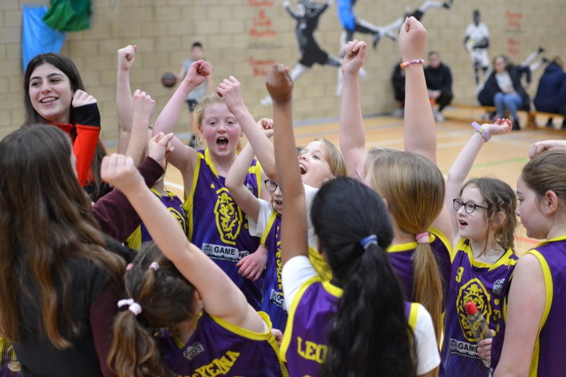 Photograph of a group of girls cheering with their arms above their heads.